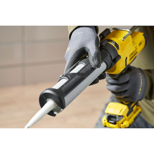 Stanley SFMCE600B pistolet à mastic sans fil tenu par une main gantée, vue rapprochée de côté.