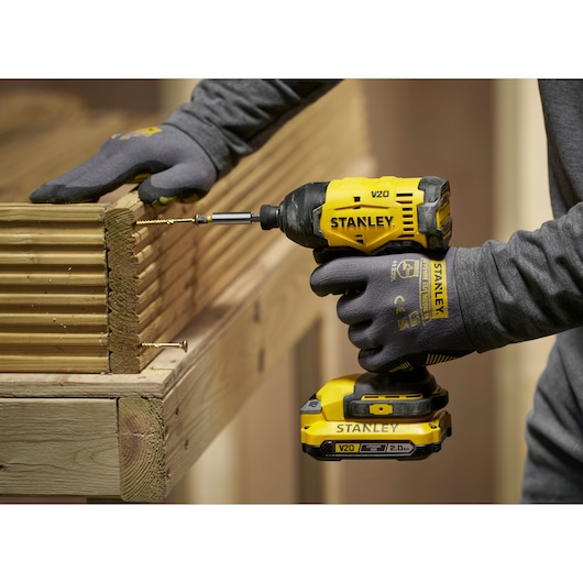 Visseuse à choc Stanley V20 sans fil insérant une vis dans des planches, personne en gants de travail.