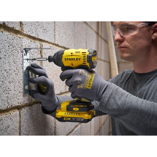 Personne utilise une visseuse Stanley V20 sans fil sur un mur, avec des gants et des lunettes de protection.