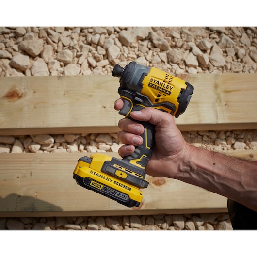 STANLEY SFMCF820D2K V20 draadloze slagschroevendraaier geel-zwart in hand gehouden, buiten.