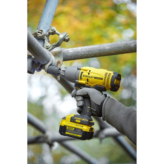 Photo de la clé à chocs STANLEY SFMCF900B utilisée sur un échafaudage, jaune et noire, batterie lithium-ion V20 4,0Ah.