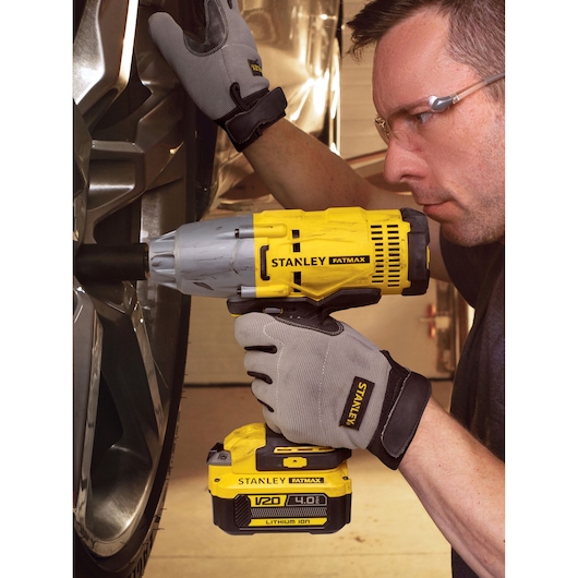 Stanley SFMCF900B clé à chocs sans fil utilisée par des mains gantées pour serrer une roue de voiture.