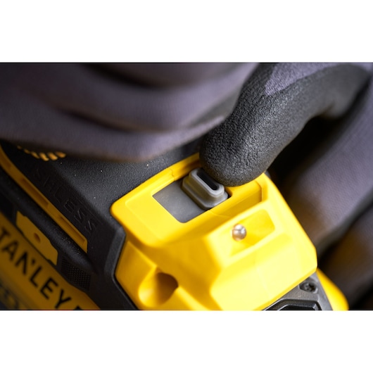 Close-up foto van STANLEY SFMCF940M1 snoerloos gereedschap met handschoen die op grijze knop drukt, geel-zwart ontwerp.