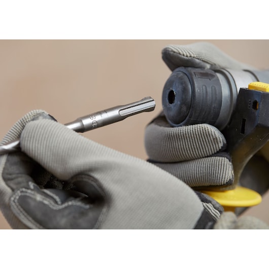 Foto van STANLEY SFMCH900B boorhamer met gehandschoende handen plaatsen een boor, close-up hoek.
