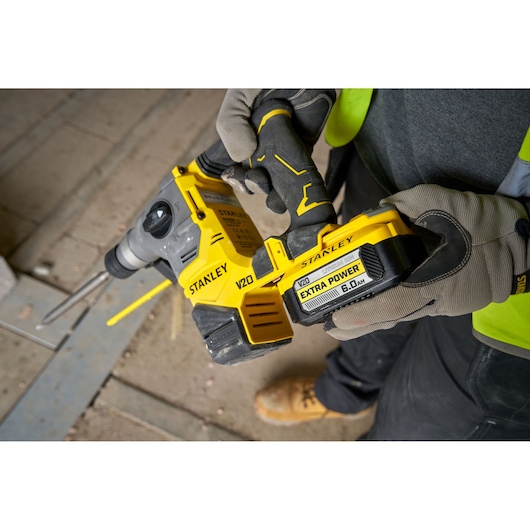 Stanley V20 draadloze boorhamer wordt vastgehouden door een persoon met handschoenen op een bouwplaats.