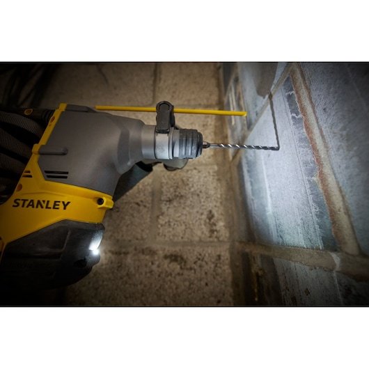 STANLEY SFMCH910R1T boorhamer boort in betonnen muur, close-up, geel en grijs gereedschap.