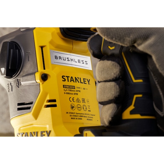 Stanley SFMCH910R1T brushless rotary hammer close-up, gele en zwarte behuizing, handschoen houdt handgreep.