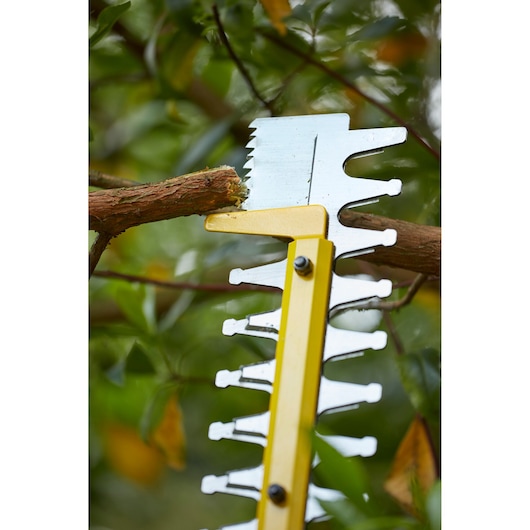Lame du taille-haie STANLEY SFMCHT855M1 en gros plan coupant une branche d'arbre à l'extérieur.