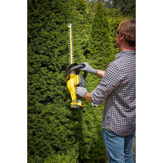 Taille-haie STANLEY SFMCHT855M1 en utilisation, personne taillant des buissons verts en extérieur.