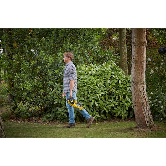 STANLEY SFMCHT855M1 taille-haie tenu par une personne marchant dehors, produit en contexte paysager.