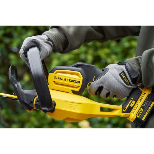 Taille-haie STANLEY SFMCHT855M1 en gros plan avec corps jaune et noir, tenu avec des gants gris en extérieur.