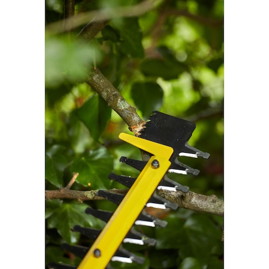 Lame de taille-haie STANLEY SFMCHTB866B coupant une branche, gros plan, fond de jardin.