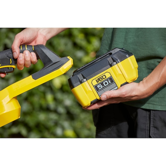 STANLEY SFMCHTB866B batterie V60 5.0Ah jaune et noire près d’un outil sans fil à l’extérieur
