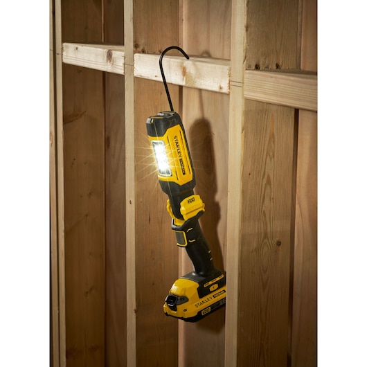 STANLEY SFMCL050B 18V STANLEY FATMAX V20 zwenklamp hangt aan houten frame, LED brandt, zwart-geel ontwerp.