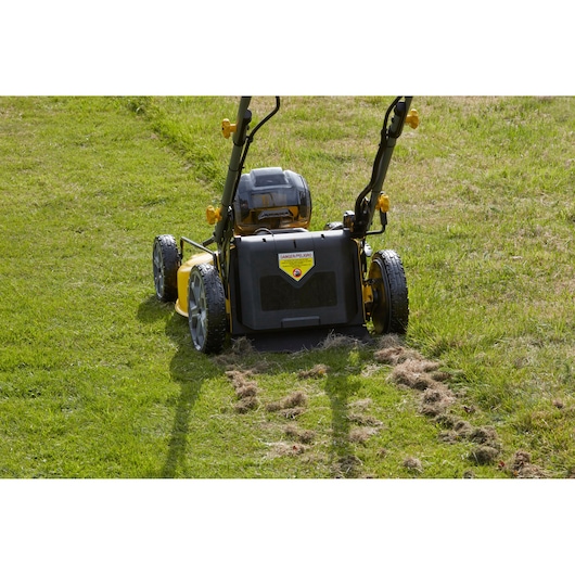 Achteraanzicht van de STANLEY SFMCMS2653B draadloze grasmaaier op gras, geel-zwart ontwerp, fotografie.