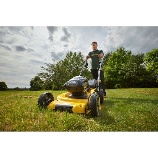 Foto van STANLEY SFMCMS2653B gele draadloze grasmaaier in gebruik op gras, vooraanzicht buiten.