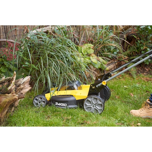 STANLEY SFMCMWS251B gele snoerloze grasmaaier in gebruik, maait gras bij planten buiten.