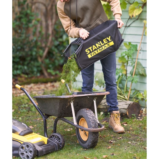 STANLEY SFMCMWS251B grasmaaier graszak wordt buiten in een kruiwagen geleegd.
