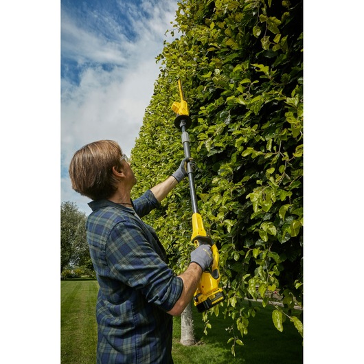 STANLEY SFMCPH845M1 telescoop-heggenschaar in gebruik, persoon snoeit hoge groene haag buiten.