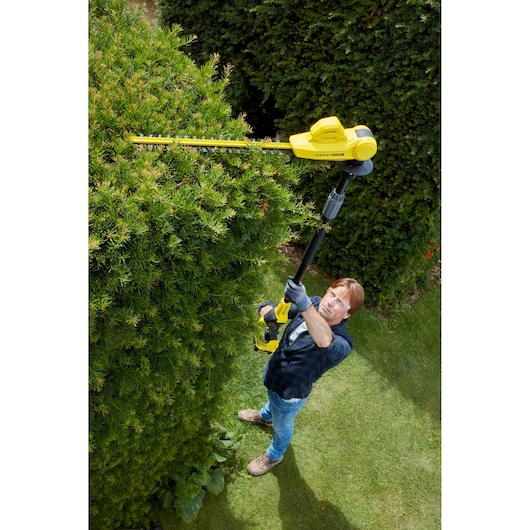 Foto van een persoon die met de STANLEY SFMCPH845M1 stokheggenschaar hoge struiken buitensnoeit.