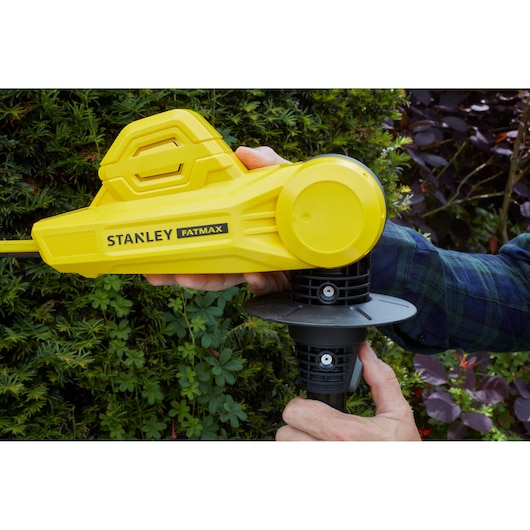 STANLEY SFMCPH845M1 gele draadloze heggenschaar in gebruik, close-up van handgreep en behuizing met tuinachtergrond.