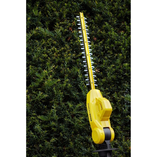 STANLEY SFMCPH845M1 heggenschaar in gebruik, geel met zwarte accenten, snoeit groene heg.