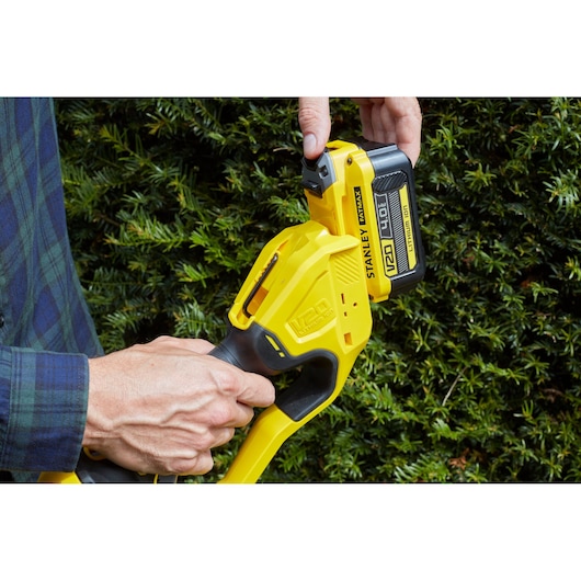 STANLEY SFMCPH845M1 heggenschaarhandvat met 18V batterij buiten getoond bij groene struiken.