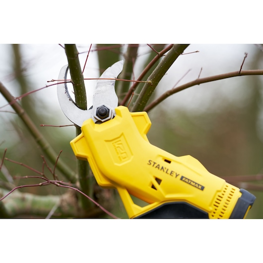 STANLEY SFMCPP32B gele snoeischaar op accu snoeit een boomtak buiten, close-up.