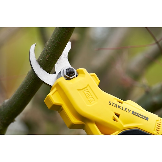STANLEY SFMCPP32B gele snoeischaar op accu knipt een tak, close-up buiten.