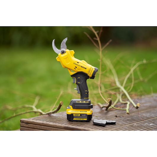 STANLEY SFMCPP32B draadloze snoeischaar op tafel buiten met takken en batterij zichtbaar.