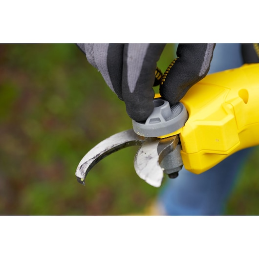 STANLEY SFMCPP32M1 gele snoeischaar close-up met gehandschoende hand die grijze knop buitenshuis aanpast.