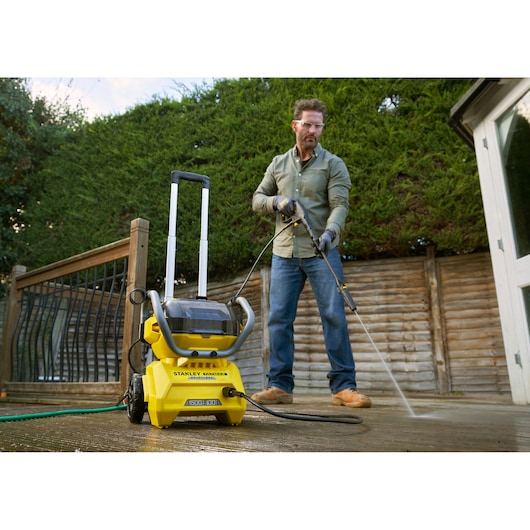 STANLEY SFMCPW1500B hogedrukreiniger op terras, gebruikt door persoon voor het schoonmaken van houten terras buiten.