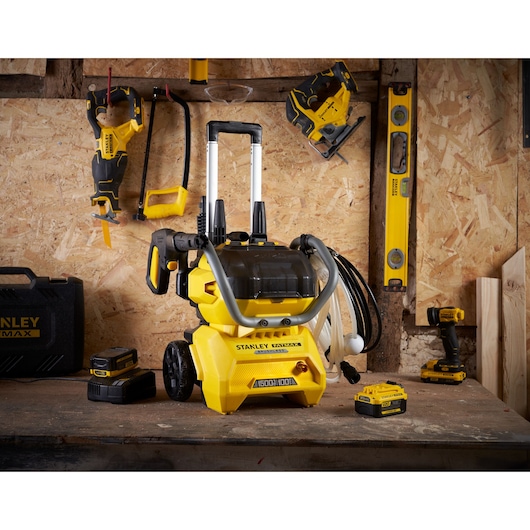 Foto van STANLEY SFMCPW1500B hogedrukreiniger op werkbank met accessoires en gereedschap in werkplaats.