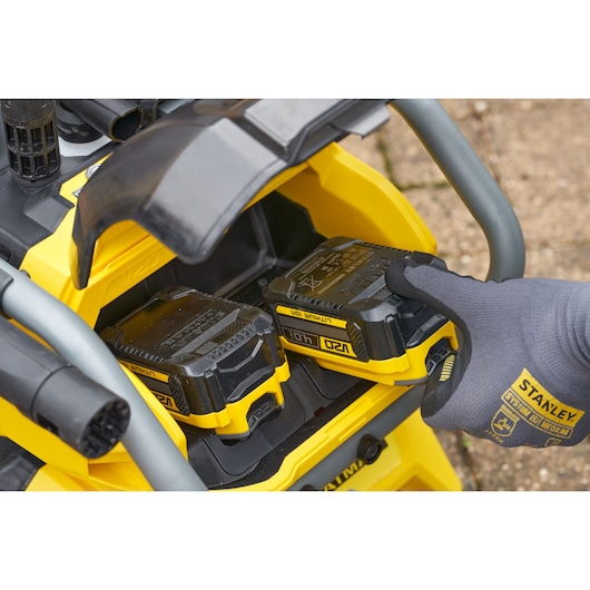 STANLEY SFMCPW1500B accuvak close-up met een gehandschoende hand die een geel-zwarte lithium-ion batterij plaatst.