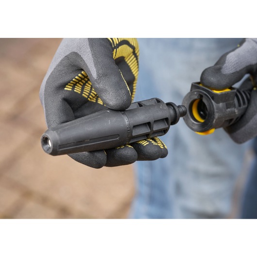 STANLEY SFMCPW1500B spuitmond opzetstuk close-up, zwart en geel, vastgehouden door handschoenen buiten.