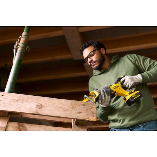 Photo d'une personne utilisant une scie sabre sans fil STANLEY SFMCS310B pour couper une poutre en bois sur un chantier.