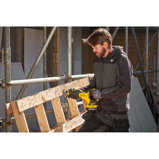 Foto van de STANLEY SFMCS311M1T reciprozaag die een houten pallet zaagt op een bouwplaats.