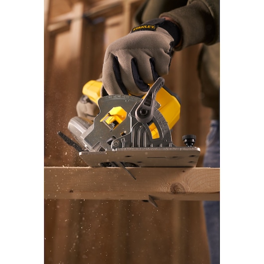 STANLEY SFMCS500B scie circulaire coupant du bois, vue latérale, design jaune et métal, environnement de chantier.