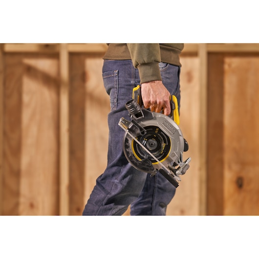 STANLEY SFMCS550M2K scie circulaire tenue par une personne, poignée jaune et noire, photo en atelier.