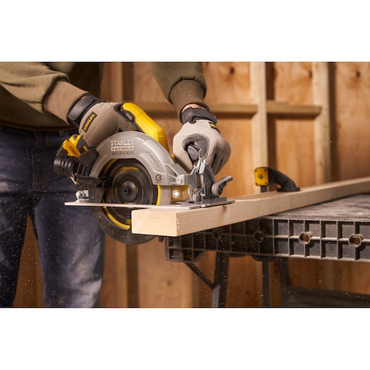 STANLEY SFMCS550M2K scie circulaire utilisée pour couper du bois en atelier, vue latérale, design jaune et argent.