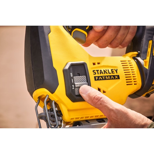 STANLEY SFMCS600B scie sauteuse en gros plan, main ajustant le bouton de réglage de vitesse sur le corps jaune et noir.