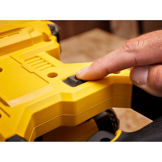 STANLEY SFMCS701M1 scie gros plan, doigt appuyant sur bouton noir sur poignée jaune.