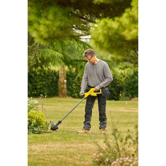 STANLEY SFMCST925B coupe-bordures utilisé par une personne pour tailler l’herbe dans un jardin, vue extérieure latérale.