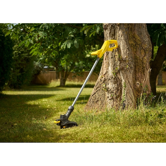 STANLEY SFMCST925B coupe-herbe sans fil sur pelouse près d'un arbre.