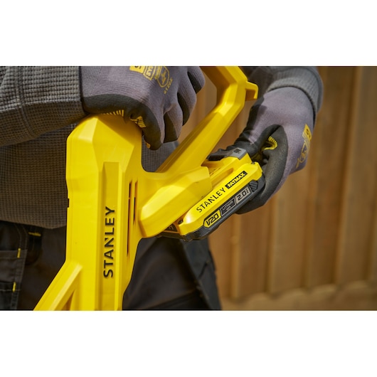 STANLEY SFMCST925B outil sans fil jaune avec batterie V20, gros plan tenu par des mains gantées.