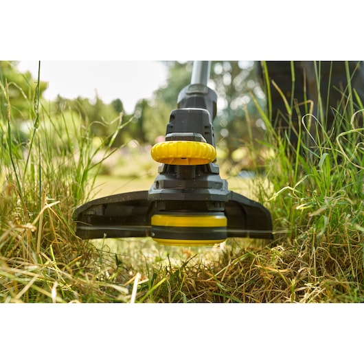 STANLEY SFMCST925M1 coupe-bordures en gros plan taillant l’herbe, tête jaune et noire utilisée en extérieur.