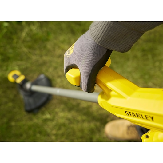 Stanley SFMCST925M1 coupe-bordures en gros plan, poignée jaune et main gantée en extérieur.