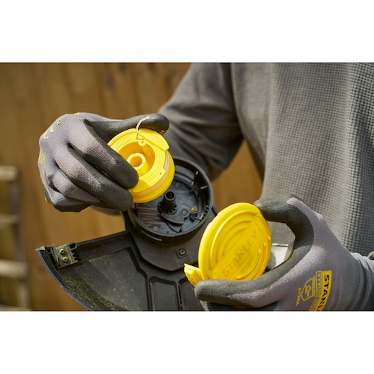 Remplacement de bobine STANLEY SFMCST925M1 pour coupe-bordures, gros plan avec pièces jaunes et gants.