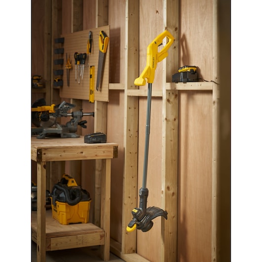 STANLEY SFMCST925M1 coupe-bordures sans fil jaune et noir, vue latérale, suspendu dans un atelier.