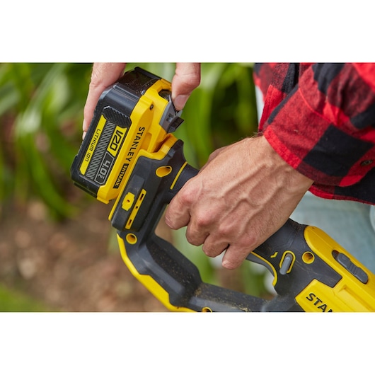 STANLEY SFMCST933B snoerloos gereedschap close-up, persoon plaatst V20 4.0Ah lithium-ion accu buiten.